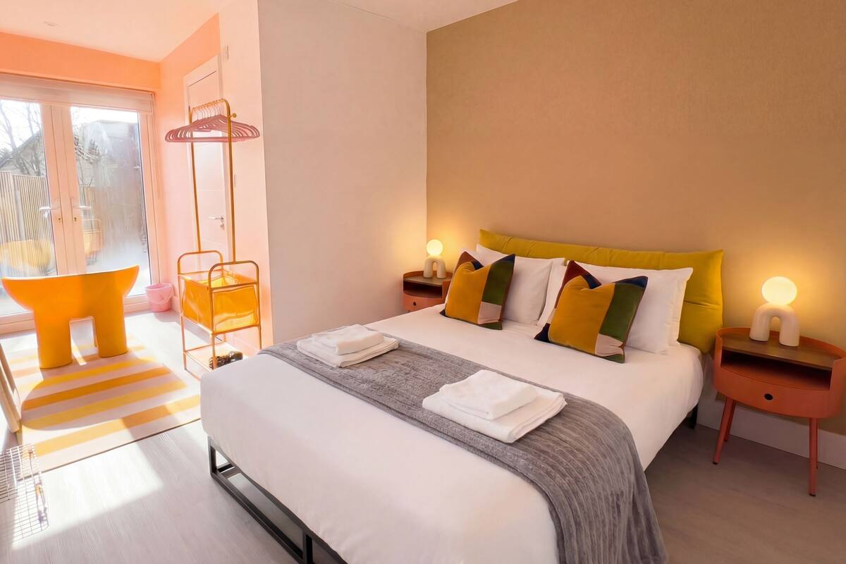 A modern hotel room with a large bed, bedside tables, a chair, and a view of the outdoors.