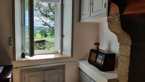 Una habitación con ventana que da a un jardín, un muro de piedra y un mueble de madera con una radio.