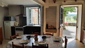 Un comedor con mesa dispuesta para cuatro, una cocina con microondas y estufa, y vista a un muro de piedra y vegetación.