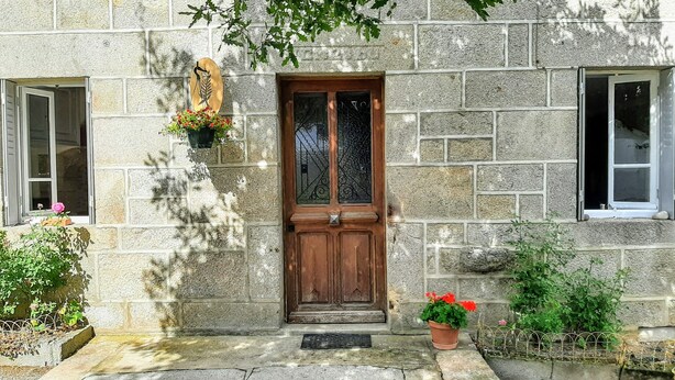 Un edificio de piedra con puerta de madera, una ventana con reja metálica y plantas en macetas.
