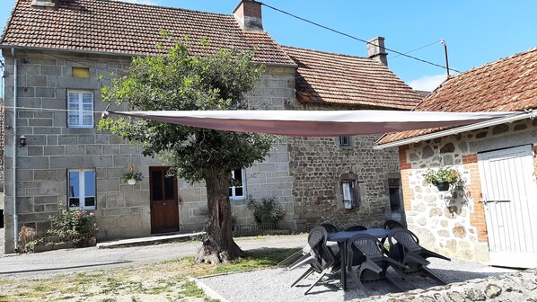 Un edificio de piedra con techo de tejas, un árbol en frente y mesas con sillas al aire libre.