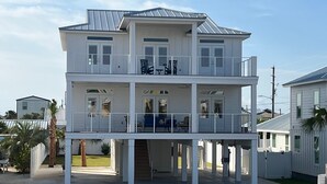 Una casa davant de la platja de dos pisos amb terrassa coberta i zona d'estar a l'aire lliure.