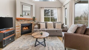 Una sala de estar moderna con chimenea de piedra, un televisor de pantalla plana grande, un sofá de cuero y una mesa de centro redonda.