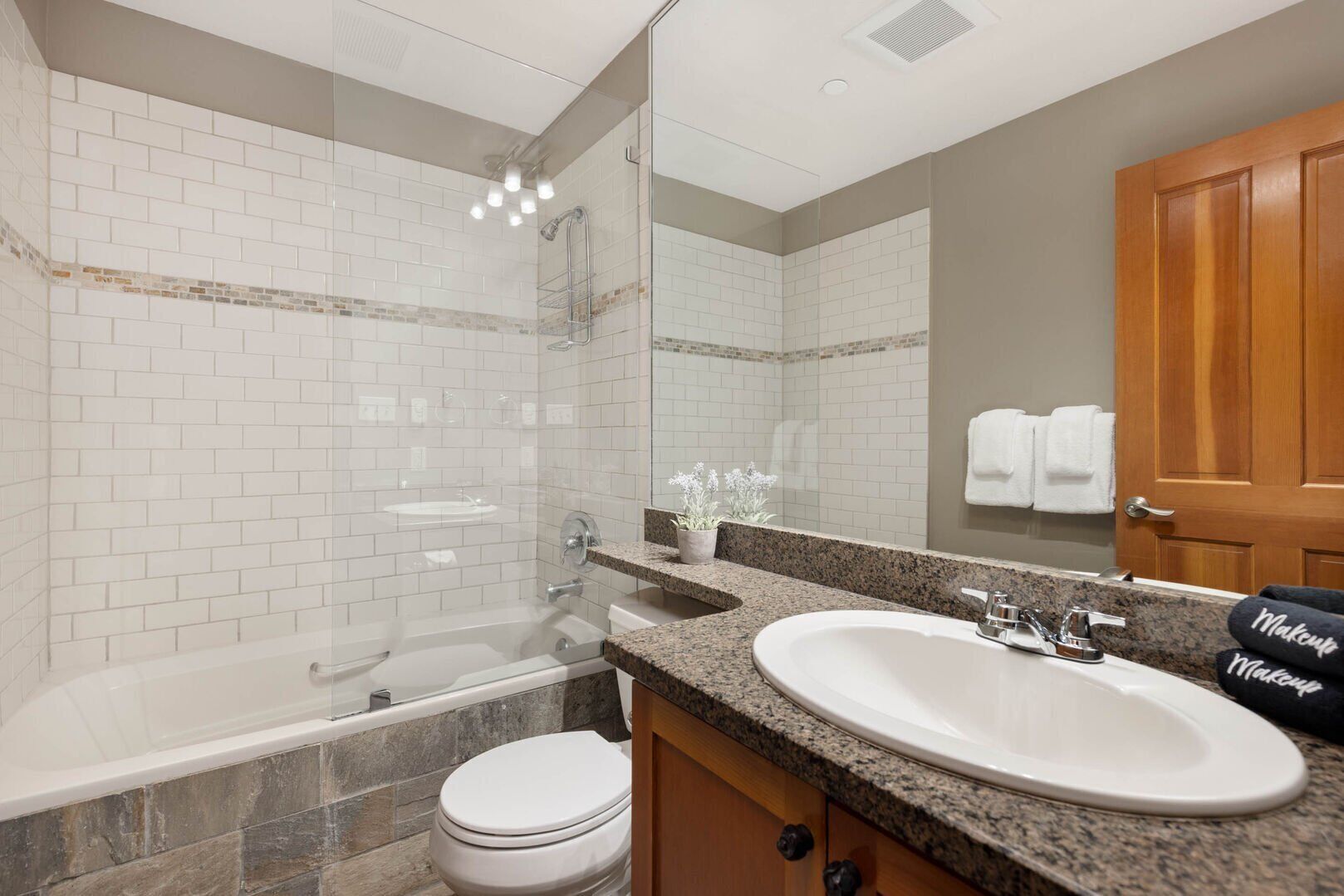 A modern bathroom with a glass-enclosed shower, a freestanding bathtub, a sink with granite countertop, and a toilet.