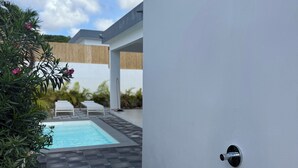 A modern outdoor shower with a pool in the background.
