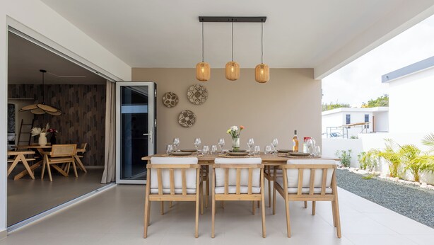 A modern dining area with a wooden table and chairs, a glass door leading to another room, and a view of the outside. - Newly built villa in prime location in Jan Thiel, pool and private parking (Willemstad)