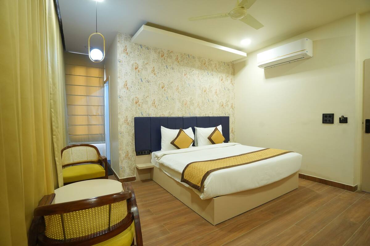 Ein Hotelzimmer mit einem Bett, zwei Stühlen, einem Deckenventilator, einer Klimaanlage und einem Fenster mit Vorhängen.