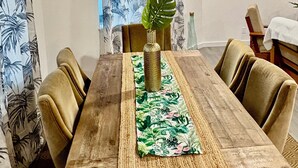 A dining table with a woven runner, surrounded by chairs, in a room with a tropical-themed curtain. - MSG host to confirm availability.• Spacious 3Bed 2BA •Sleeps 10 (Laie)