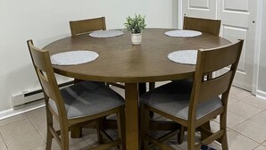 A round wooden dining table with four chairs, each with a grey cushion. A small potted plant is on the table.