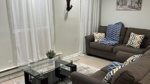 A living room with a glass coffee table, a sofa with patterned cushions, and a framed picture on the wall.