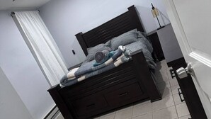 A bedroom with a dark wooden bed, a white curtain, and a bedside table with a lamp.