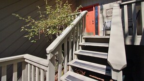 A wooden staircase with a railing, a plant, and a red door.