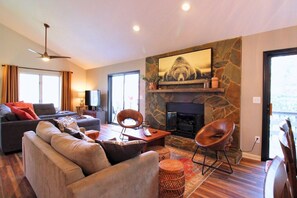 Una sala de estar con sofá, sillas, chimenea, televisor y pared de piedra.