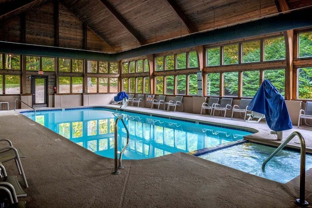 Ein Hallenbad mit Holzbalkendecke, Fenstern und Liegestühlen.