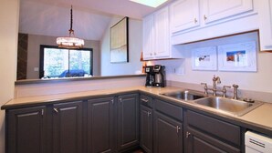 A modern kitchen with dark cabinets, a stainless steel sink, a coffee maker, and framed pictures on the wall.