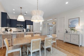 A modern kitchen with dark cabinets, a wooden island, and a dining area with wicker chairs. - 30A | 2 Mins to Beach | Private Pool & Beach! (Inlet Beach)