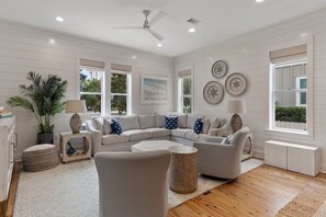 A modern living room with a sectional sofa, a ceiling fan, and a large window with blinds. - 30A | 2 Mins to Beach | Private Pool & Beach! (Inlet Beach)
