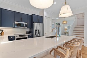 Cocina moderna con armarios azul oscuro, electrodomésticos de acero inoxidable, encimera de mármol blanco y una zona de bar con sillas de mimbre.