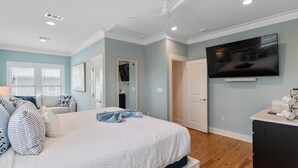 Una camera da letto con un letto, un ventilatore a soffitto, un televisore e l'ingresso del bagno.