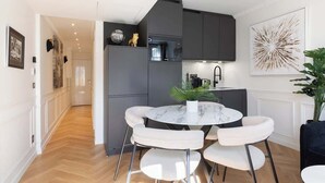 Una cocina moderna con armarios oscuros, una mesa redonda de mármol y sillas blancas.
