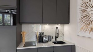 Una cocina moderna con armarios oscuros, encimera de mármol, un lavamanos, un tostador y una tetera.