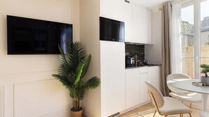 Una cocina moderna con armarios blancos, un televisor de pantalla plana montado en la pared y un comedor con mesa redonda y sillas.
