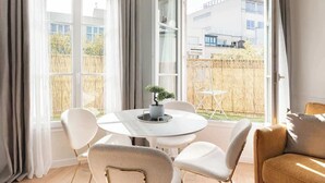 Una habitación luminosa con una mesa redonda, sillas blancas y una planta en maceta.