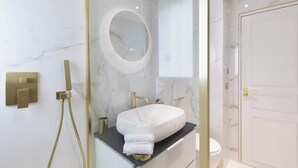 Un baño moderno con un lavabo de mármol, un espejo redondo y una ducha con cerramiento de vidrio.