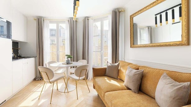 Una sala moderna con un sofá, una mesa de comedor con sillas y un espejo grande en la pared.