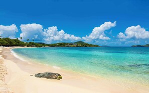 A beach with clear turquoise water, a sandy shore, and a large rock in the foreground.
