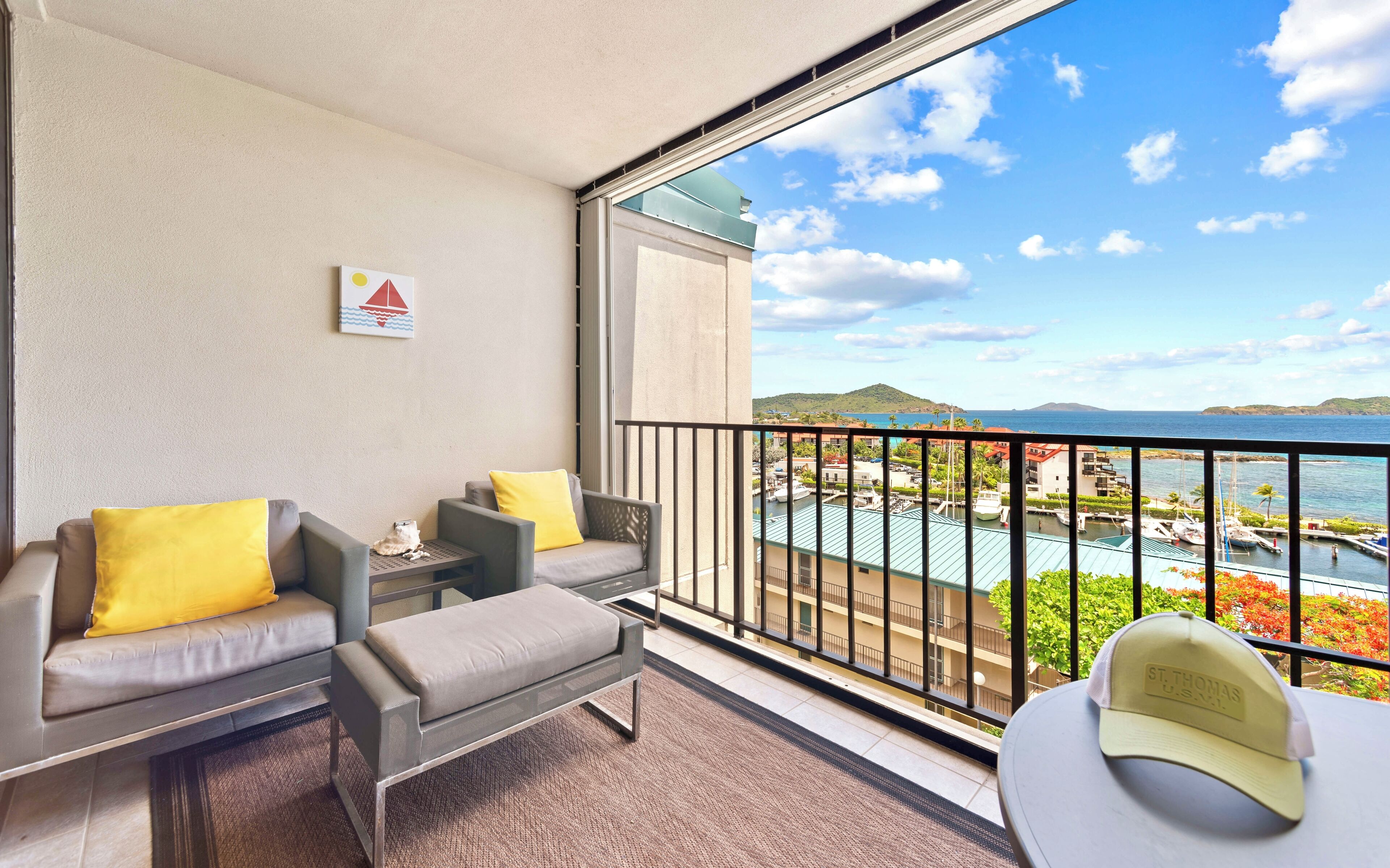 A balcony with a sofa and armchair, a small table, and a view of the sea and buildings.