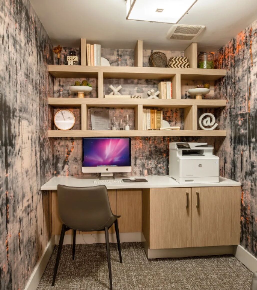 A home office with a desk, chair, computer, printer, and shelves with books and decorative items.