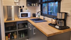 A modern kitchen with a microwave, sink, and coffee maker. There is a window with blinds and a clock on the wall. - The TINY HOUSE at Le Haras. (Avrillé)