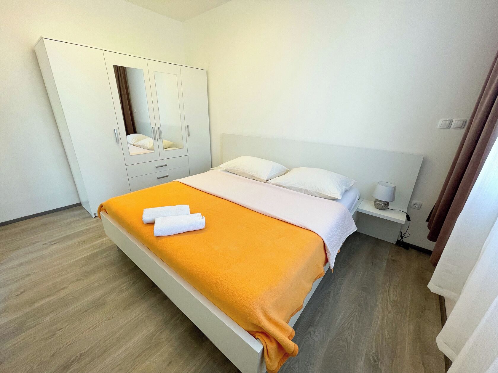 A hotel room with a bed, a wardrobe, a bedside table, and a lamp.