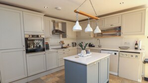 Een moderne keuken met een centraal eiland, een ingebouwde oven en hangende lampen.