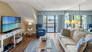 Un salon avec une télévision, un fauteuil bleu, un canapé beige et un balcon avec vue.
