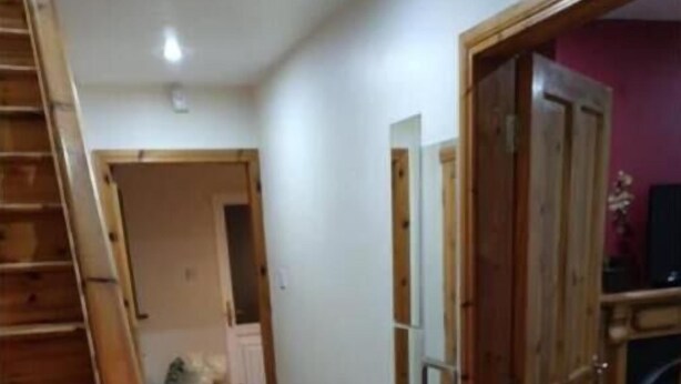 Un pasillo con escalera de madera, suelo de baldosas y una puerta con espejo.