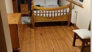 Un dormitorio con cama de madera, una mesita de noche, una silla y un ventanal con persiana.