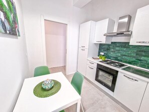 Een koelkast, een oven, kookgerei, borden en bestek, een eettafel
