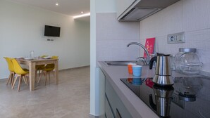 A modern kitchen with a stainless steel kettle, a sink, and a flat-screen TV mounted on the wall.