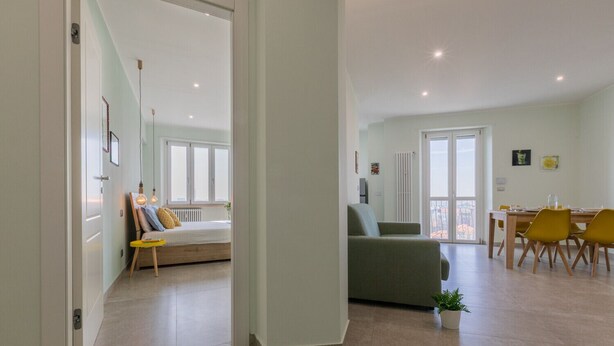 A spacious living area with a sofa, a dining table with chairs, and a view through a glass door.