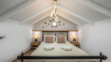 A bedroom with a high ceiling, a bed with two pillows, bedside tables with lamps, and a hanging light fixture.