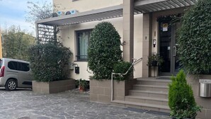 A modern two-story house with a stone-paved entrance, a car parked on the left, and a well-maintained garden with potted plants. - 12. Apartment (Signa)