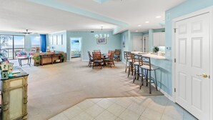 A spacious living area with a dining table and chairs, a kitchen area with bar stools, and a large window with a view.