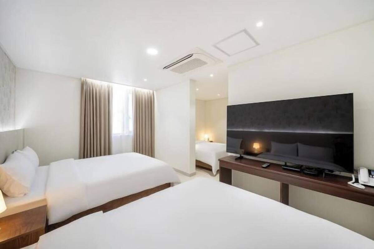 A hotel room with two beds, a flat-screen TV, a desk with a phone, and a window with curtains.