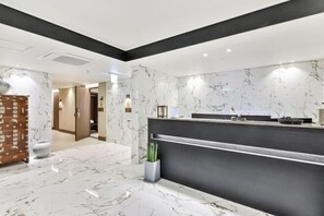 A hotel lobby with a reception desk, marble flooring, a plant, and a wooden cabinet. - hotel onggi (Gyeongju)
