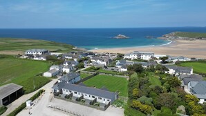 A coastal residential area with houses, a beach, and a rocky outcrop in the distance. - Atlantic View Chalets #2 | Self-catering holiday cottage near Crantock beach (Crantock)