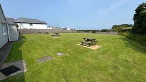 A well-maintained grassy backyard with picnic tables and a wooden fence. - Atlantic View Chalets #2 | Self-catering holiday cottage near Crantock beach (Crantock)