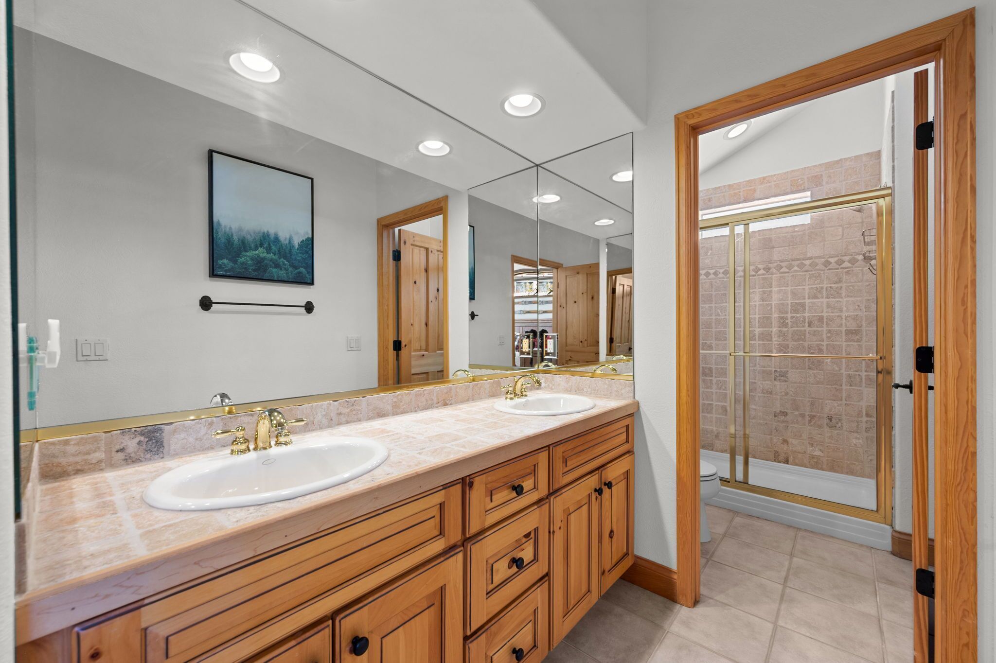 A modern bathroom with two sinks, wooden cabinets, a large mirror, and a glass shower enclosure.