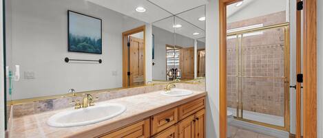 A modern bathroom with two sinks, wooden cabinets, a large mirror, and a glass shower enclosure.